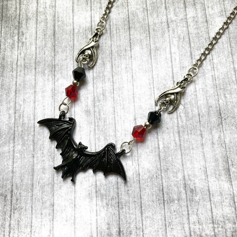 Necklace with a bat pendant and red and black beads on a wooden surface