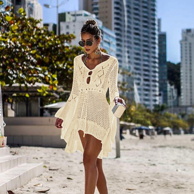Woman in a Beige crochet cover-up on a beach with cityscape in the background