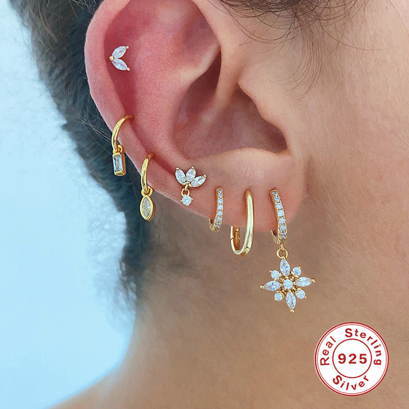 Close-up of an ear with gold and silver earrings, featuring a 'Real Sterling Silver' stamp.