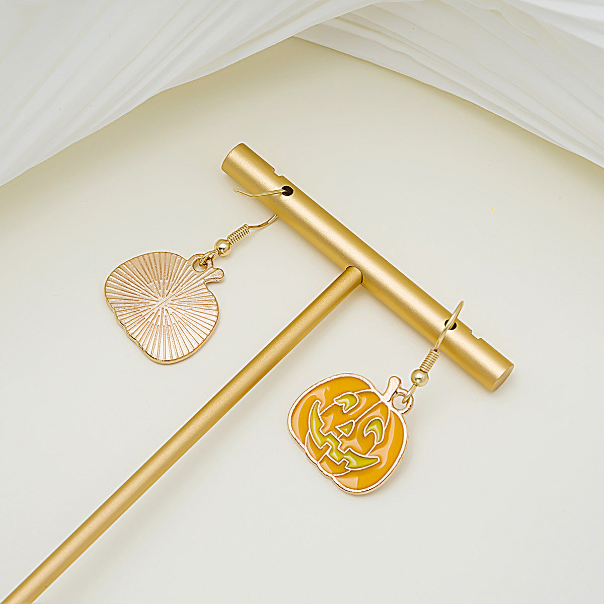 Gold earrings with leaf and pumpkin design on a light background