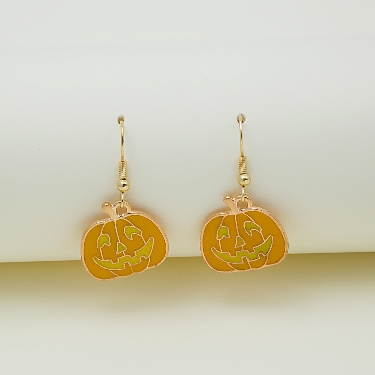 Gold pumpkin-shaped earrings on a light beige background