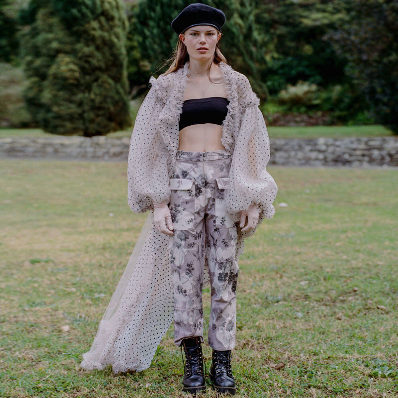 Woman in a polka dot cover up and patterned outfit standing in a grassy area with trees in the background