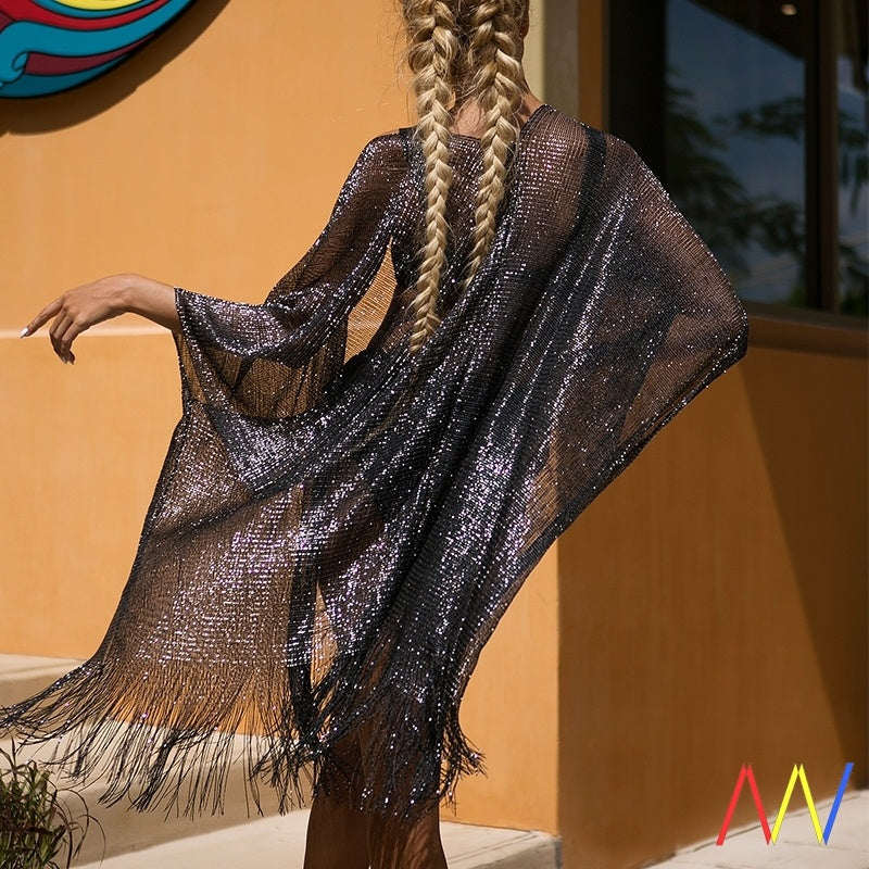 Person wearing a black shimmery cover-up with fringe, standing against an orange wall.
