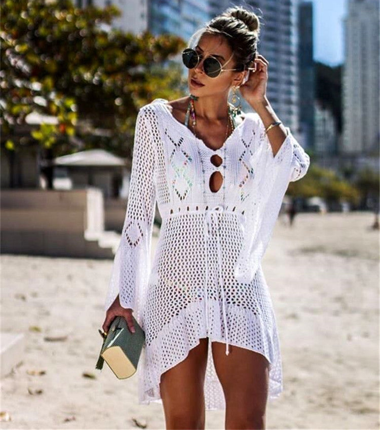 Woman wearing a white crochet cover-up on a beach with buildings in the background