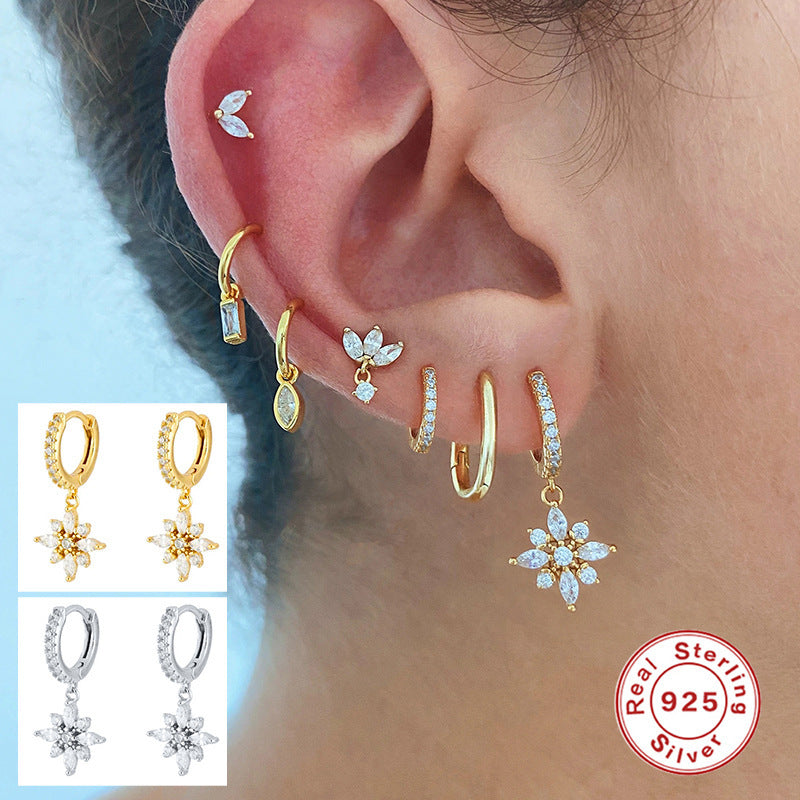 Close-up of an ear wearing gold and silver earrings with a 'Real Sterling Silver' stamp.