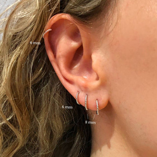 Close-up of an ear wearing two silver hoop earrings with size labels.