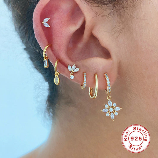 Close-up of an ear with gold and silver earrings, featuring a 'Real Sterling Silver' stamp.