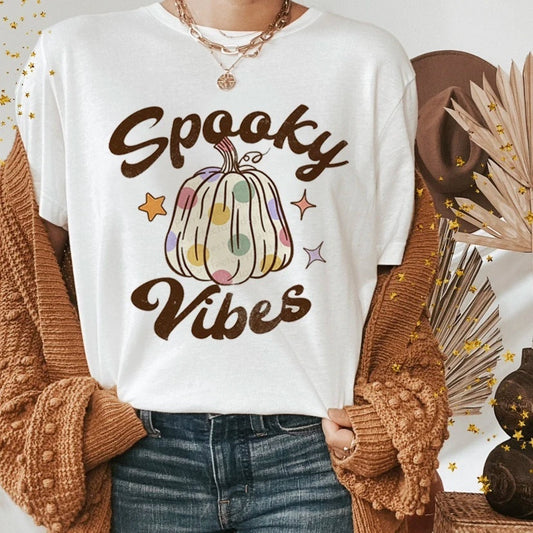 Person wearing a white t-shirt with a colorful pumpkin design and 'Spooky Vibes' text, standing against a neutral background.