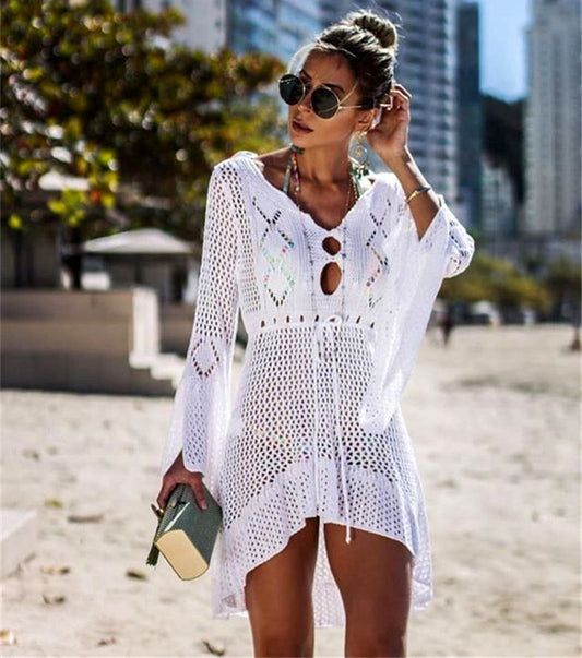 Woman wearing a white crochet cover-up on a beach with buildings in the background